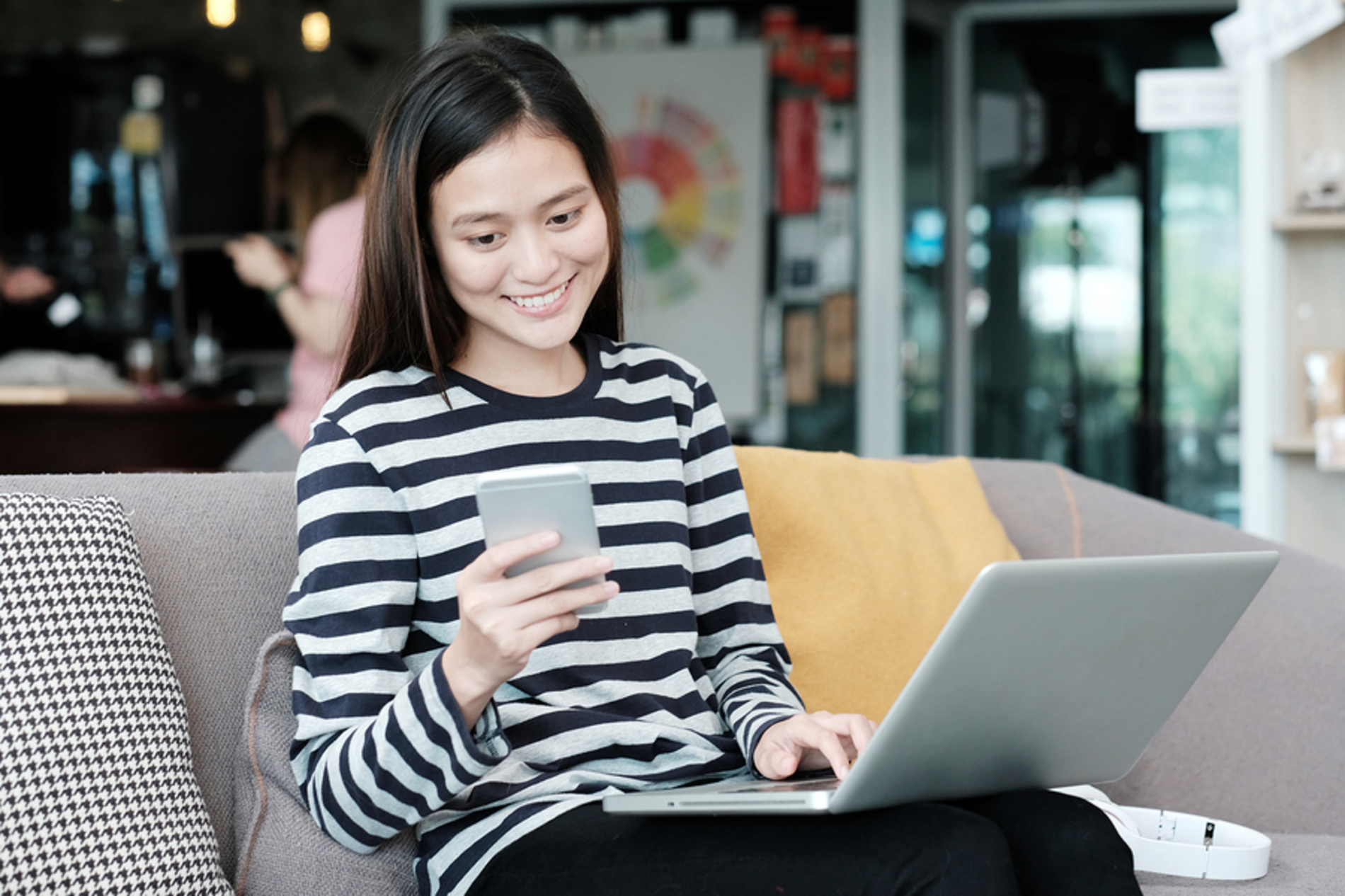 Woman sitting on a couch with her laptop and looking at her phone.